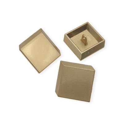 Três tampas quadradas douradas com textura, uma virada ao contrário mostrando pino interior