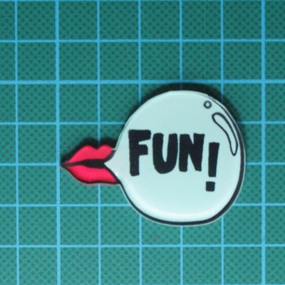 Emblema branco com FUN! e lábios vermelhos sobre superfície verde com grelha azul