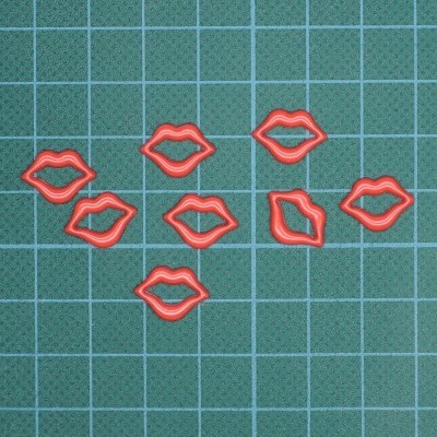 Clips de papel vermelhos em forma de lábios sobre superfície de corte verde