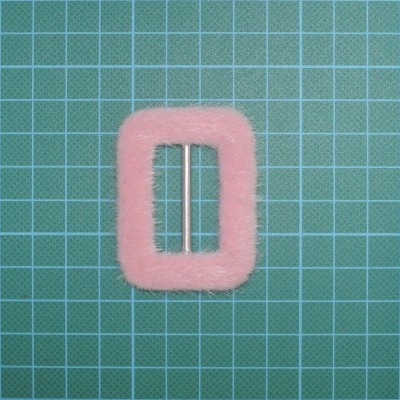 Fivela rosa peluda retangular com barra metálica sobre superfície verde quadriculada