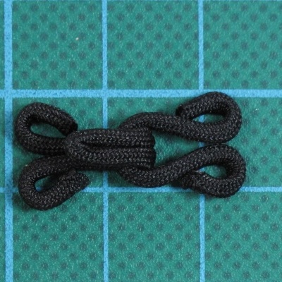 Fecho de cordão preto com argolas em superfície verde quadriculada.