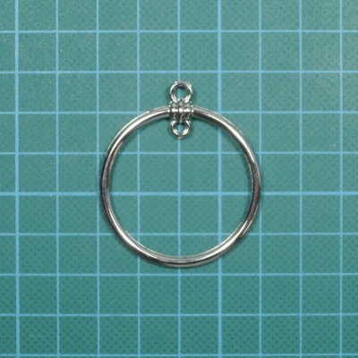 Argola metálica prateada circular com pequeno anel no topo sobre fundo de grelha verde