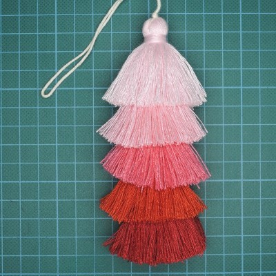 Pendurador de franjas em tons degradé de rosa a vermelho sobre superfície de corte com grade