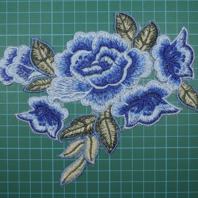 Aplicação bordada azul e verde sobre superfície de corte verde.