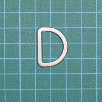 Argola em D de plástico branco sobre superfície de corte azul com grelha quadriculada.