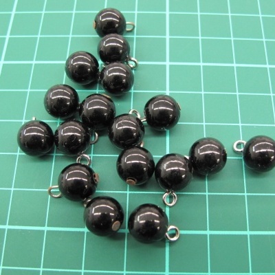 Esferas pretas com ganchos metálicos sobre superfície verde com grelha branca