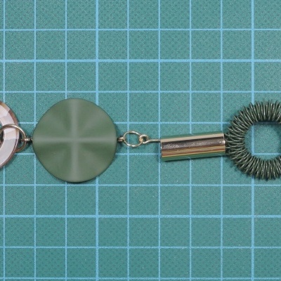 Pulseira metálica com elos prateados e detalhes verdes sobre fundo quadriculado verde