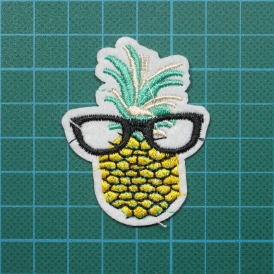 Emblema bordado de ananás com óculos sobre superfície verde quadriculada