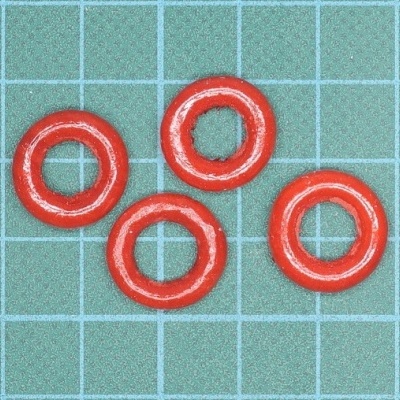 Anéis de vedação vermelhos dispostos sobre superfície quadriculada verde.