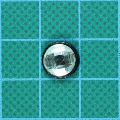 Botão redondo transparente facetado com base preta sobre papel quadriculado verde