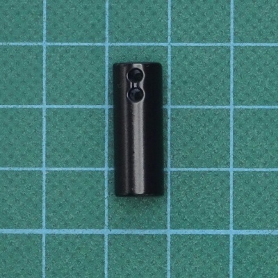 Peça cilíndrica preta com dois orifícios sobre fundo quadriculado verde