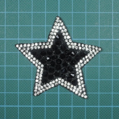Estrela decorativa preta com borda de strass prateados sobre fundo quadriculado verde