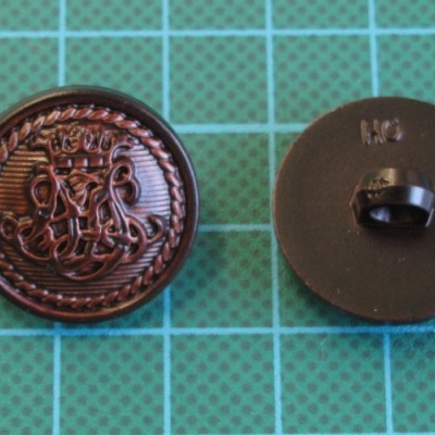 Dois botões redondos, um cobre com gravação detalhada e outro preto, sobre fundo quadriculado verde.