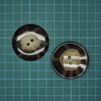 Dois botões redondos em tons pele e castanho com dois furos sobre fundo azul com grelha