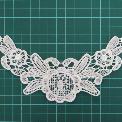 Aplicação renda branca floral detalhada sobre fundo verde quadriculado