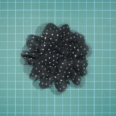 Flor de tecido preto com pontos brancos sobre fundo quadriculado verde