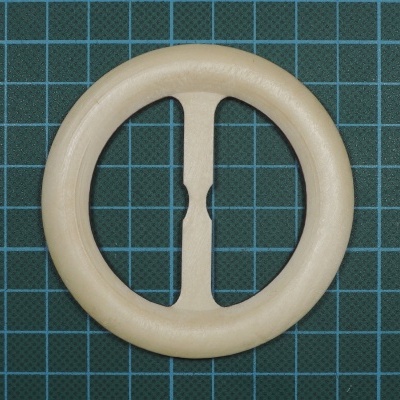 Fivela circular clara com dois braços verticais ao centro sobre superfície de corte verde quadriculada