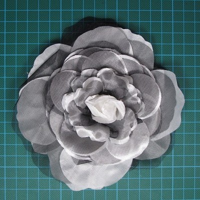 Flor decorativa artificial cinza e branca em tecido sobre fundo quadriculado azul-esverdeado