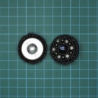 Dois botões redondos pretos com pedras brilhantes e base metálica sobre fundo verde quadriculado
