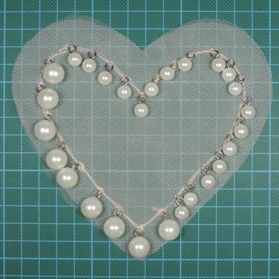 Colar de pérolas em forma de coração sobre malha transparente em fundo verde quadriculado