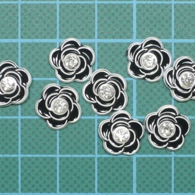 Oito botões florais preto, branco e metalizado com detalhe brilhante no centro sobre fundo verde quadriculado
