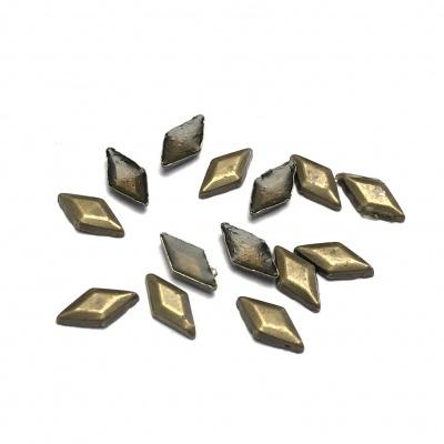 Peças metálicas douradas em forma de losango com superfície oxidada numa base branca