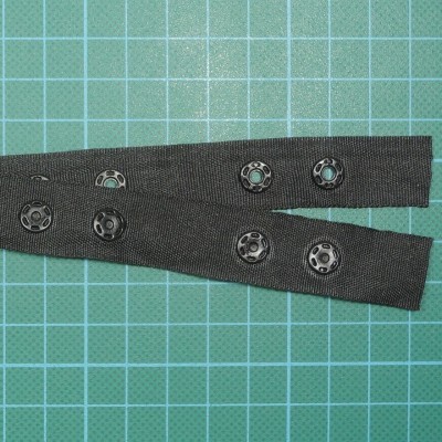 Tiras pretas com botões de pressão sobre superfície azul de grelha