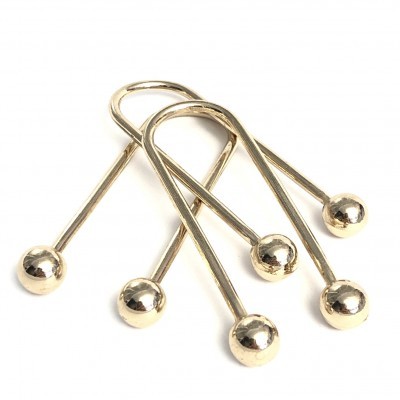 Quatro ganchos metálicos dourados com bolas nas extremidades sobre fundo branco