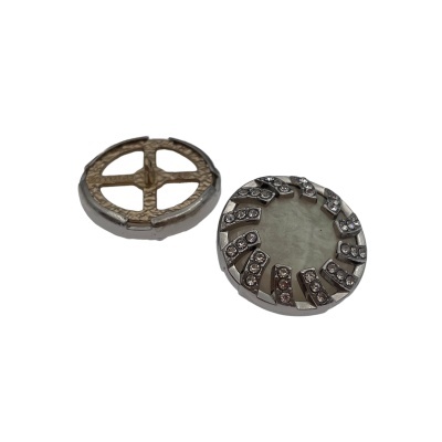 Dois botões redondos em metal prateado com padrões distintos e pedras brilhantes.