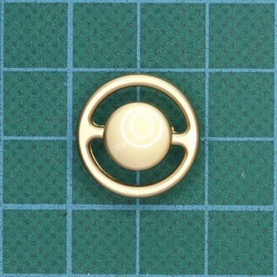 Botão redondo creme e dourado sobre superfície verde quadriculada