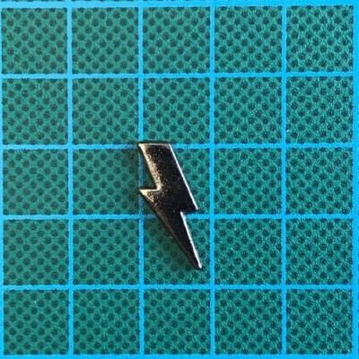 Íman metálico em forma de raio sobre superfície verde quadriculada azul