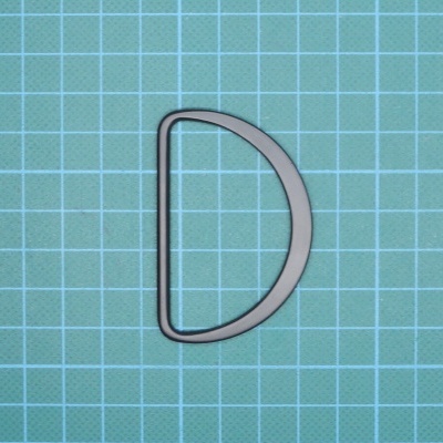 Fivela metálica em forma de D sobre superfície de corte azul com grade quadriculada branca