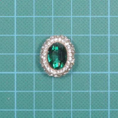 Anel com pedra verde oval e pedras brancas ao redor sobre fundo verde quadriculado