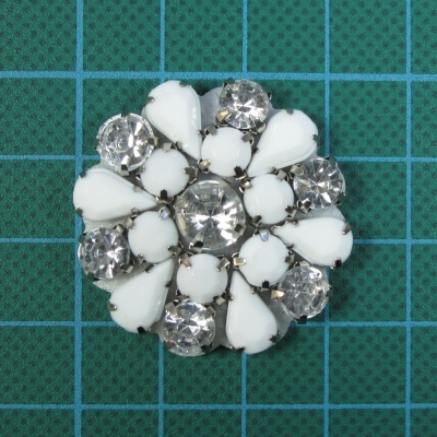 Broche redondo com pedras brancas e transparentes em suporte metálico prateado