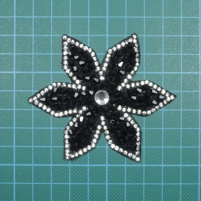 Aplicação decorativa em forma de flor preta com cristais e contorno prateado sobre base verde
