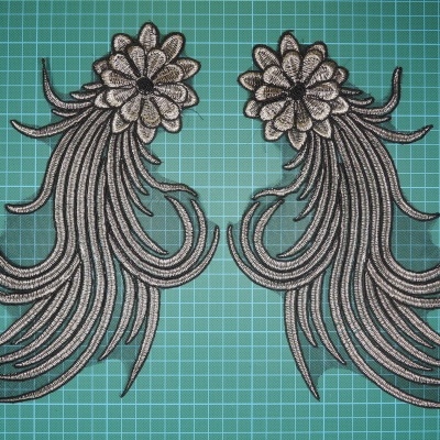 Dois apliques de flores prateadas com detalhes em preto sobre base verde quadriculada