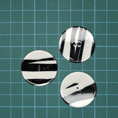 Três botões redondos preto e branco com dois orifícios sobre superfície verde com grade branca