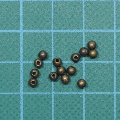 Contas esféricas de bronze metálico com furo central sobre superfície verde quadriculada azul claro