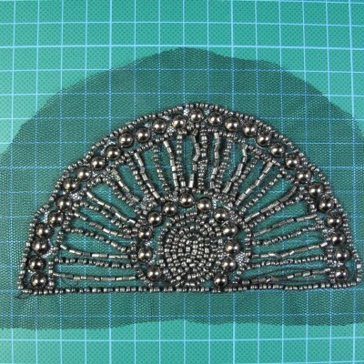 Acessório semicircular azul com contas prateadas sobre superfície quadriculada verde