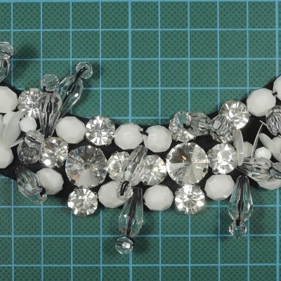 Peça de bijuteria com pedras transparentes e esferas brancas sobre fundo verde quadriculado
