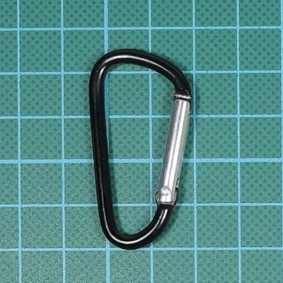 Mosquetão metálico preto e prata sobre superfície verde quadriculada