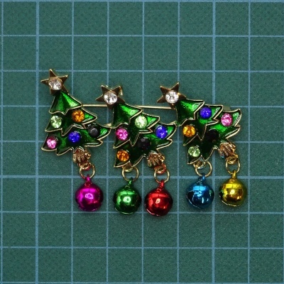 Pins decorativos de árvore de Natal com pedras coloridas e sinos sobre fundo quadriculado verde