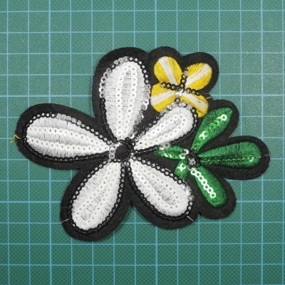 Aplique em tecido com flores em lantejoulas prateadas, amarelas e verdes sobre base de corte verde