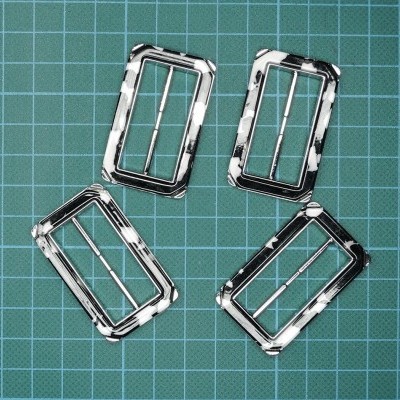 Quatro fivelas retangulares metálicas com padrão preto e branco sobre fundo quadriculado