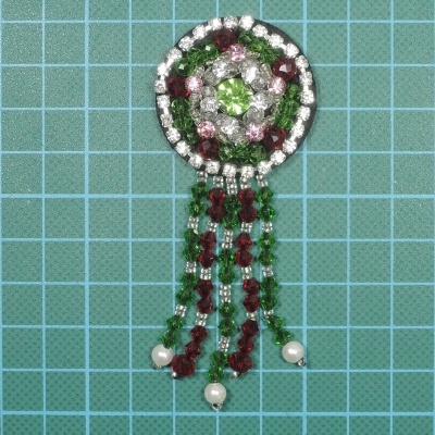 Broche decorativo com pedras e franjas em fundo azul com grade.