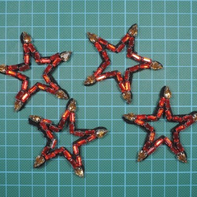 Quatro estrelas decorativas feitas com pequenas luzes vermelhas e transparentes sobre fundo quadriculado verde