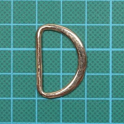 Argola metálica dourada em formato de D sobre fundo azul com grade