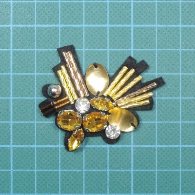 Aplicação decorativa com pedras âmbar e transparentes e detalhes dourados sobre fundo azul quadriculado