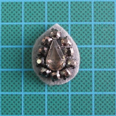 broche com pedras em tecido cinzento sobre fundo quadriculado verde