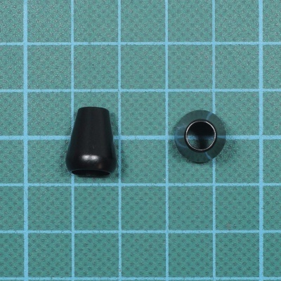 Dois pequenos acessórios de plástico preto sobre fundo verde com grade azul clara